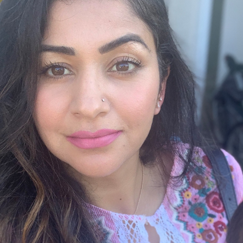 woman with long dark brown hair, and brown eyes wearing a floral patterned pink shirt