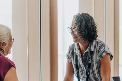 Two women standing on either side of a desk. They are engaged in conversation and are smiling at each other