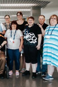 A group of people standing for a photo. They are in a large indoor space brightly lit by daylight