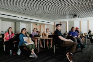a group of people seated at round tables watching the front of a room